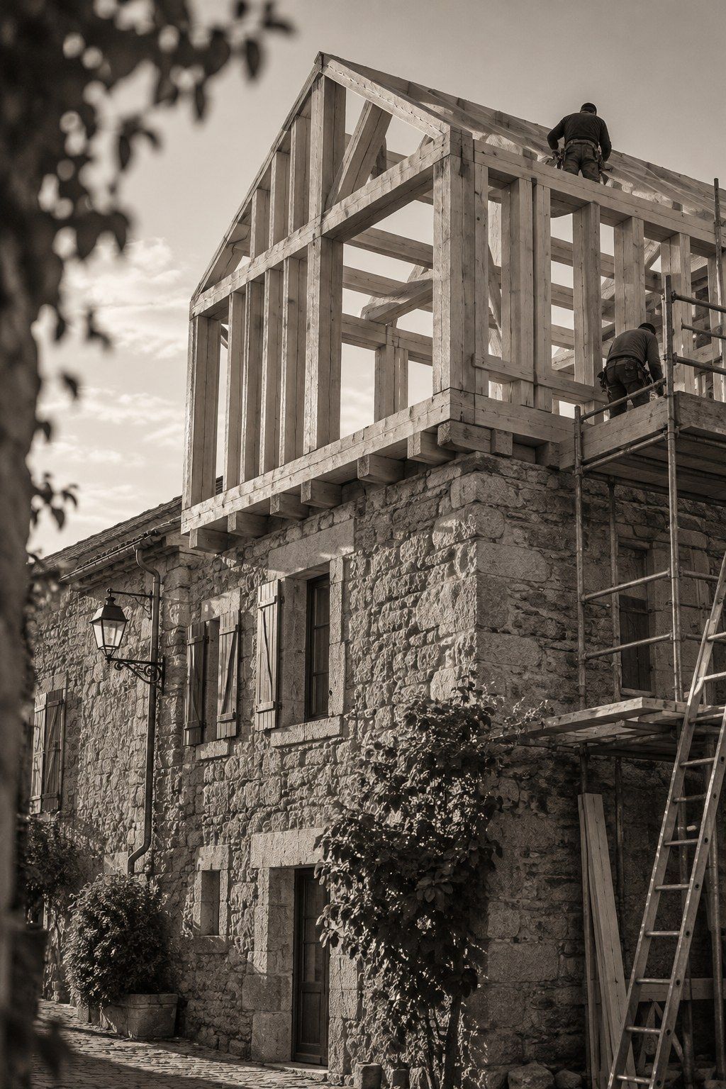 Nouvel étage à ossature bois monté sur une maison ancienne en pierre, charpentiers sur l’échafaudage